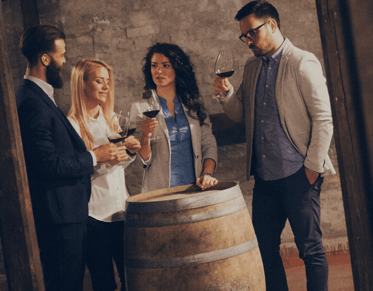 group of people gather around wine barrels for barrel tasting